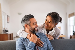 Smiling woman hugging her husband on the couch from behind in the living room