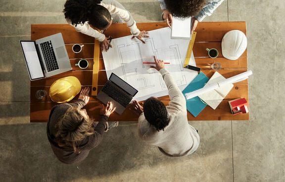 Top down view of four architects working on blueprints on a desk
