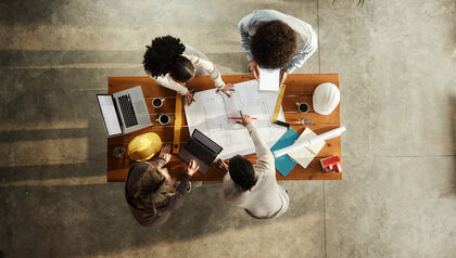 Top down view of four architects working on blueprints on a desk