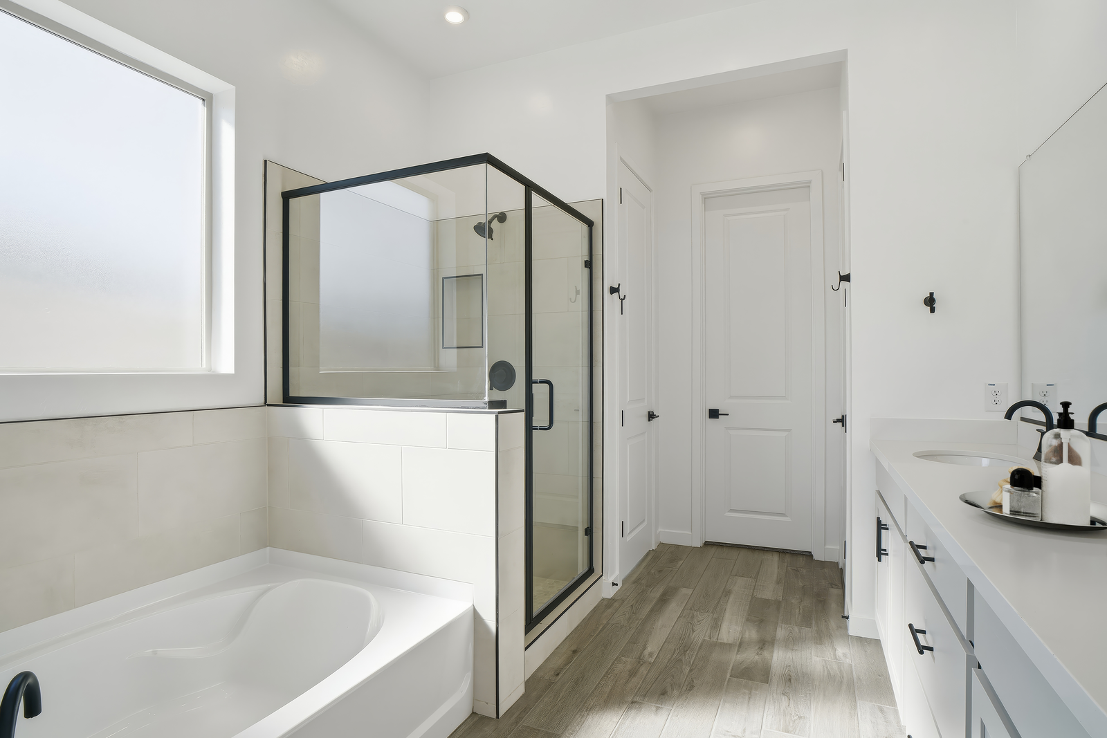 bathroom with wood-like flooring, soaking tub, and walk-in shower with black hardware