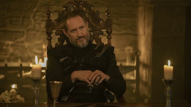 Bertie Carvel as Prince Baelor “Breakspear” Targaryen seated on a throne in front of a fireplace inside a stone hall in A Knight of the Seven Kingdoms.