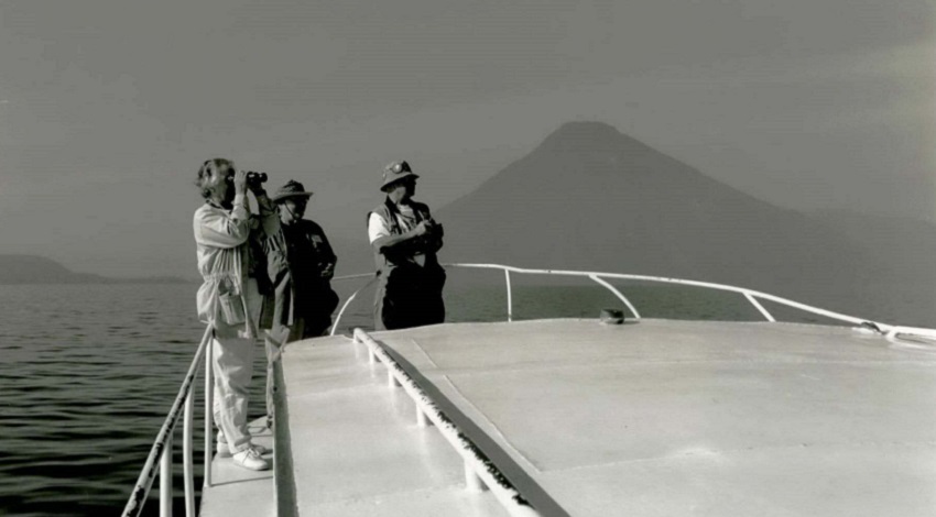 A black and white photo of Road Scholars at the front of a ship with a tall mountain in the background