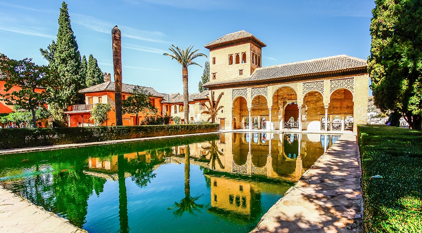 A colorful courtyard with lush plants and a reflective pool in Spain