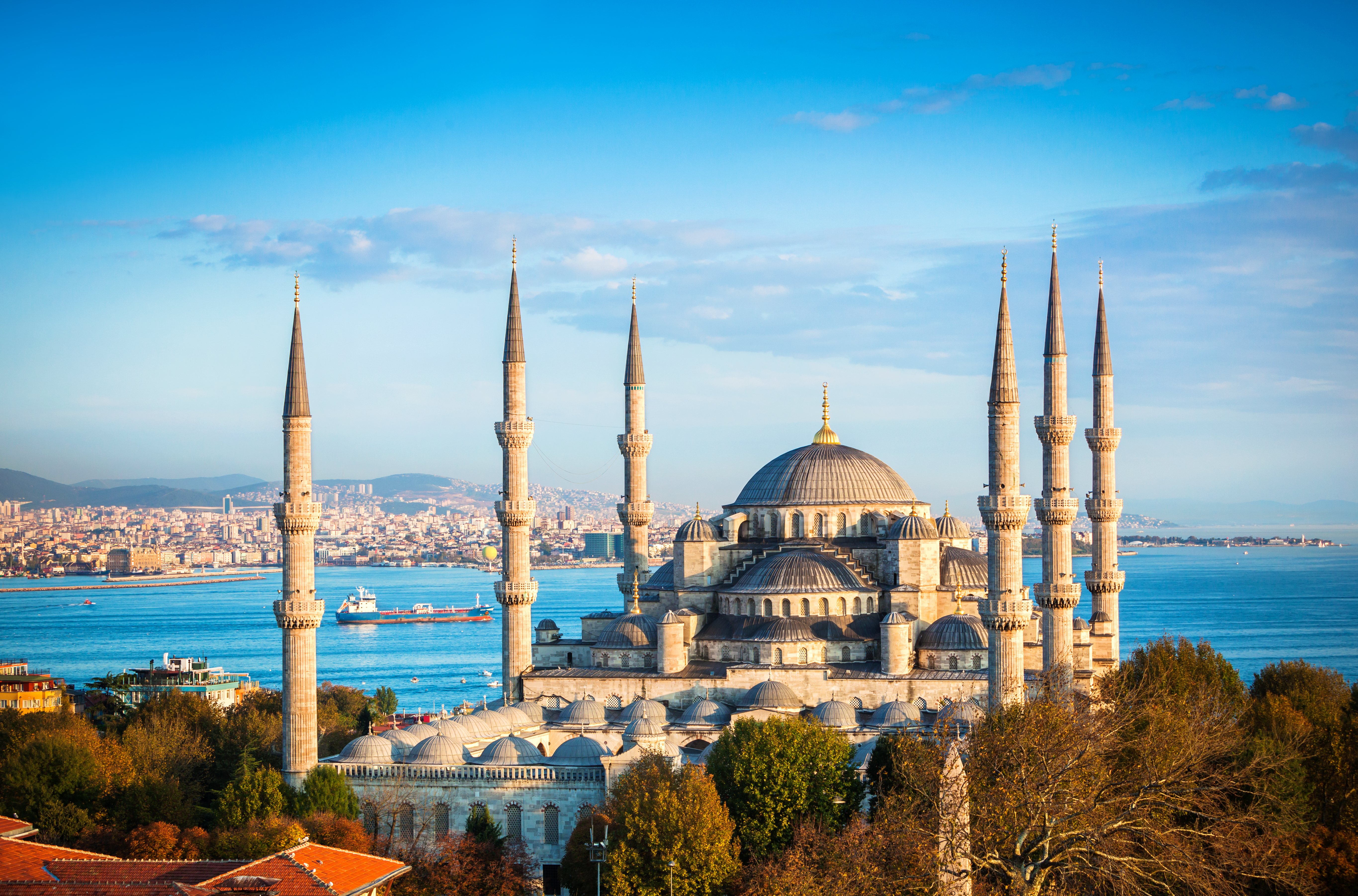 The Blue Mosque in Istanbul features its iconic domes and six minarets overlooking the Bosphorus waterway under a clear blue sky.