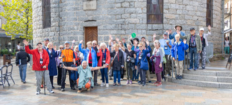 Road Scholar Peg J. and a group of friends wave while standing in front of a historic stone building in Corsica.
