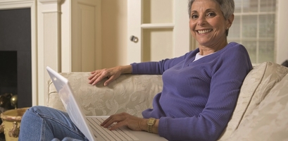 A woman smiles while scrolling through her laptop computer