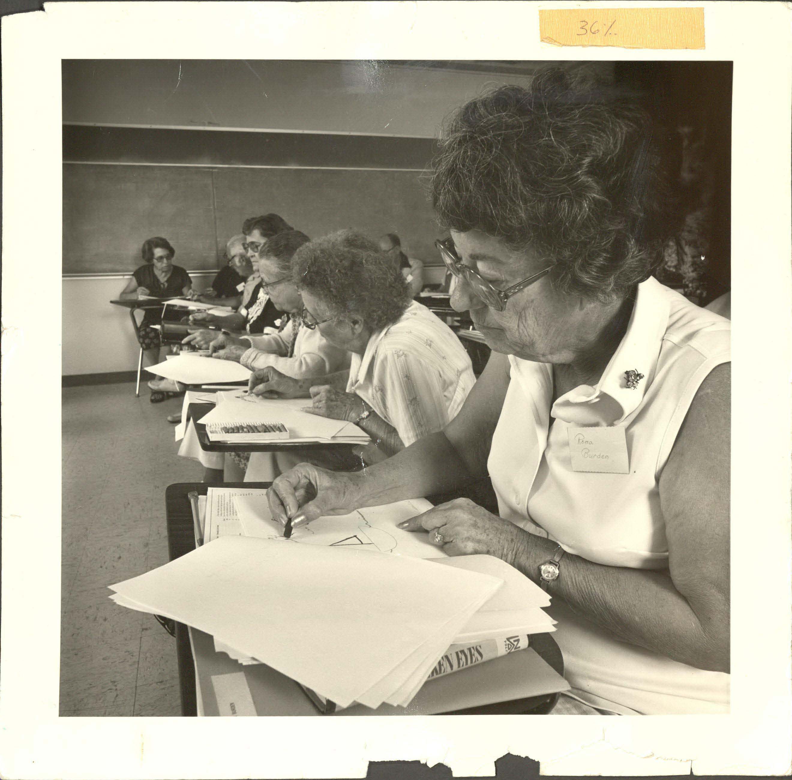 An older photo of women sitting at a line of desks working through stacks of papers