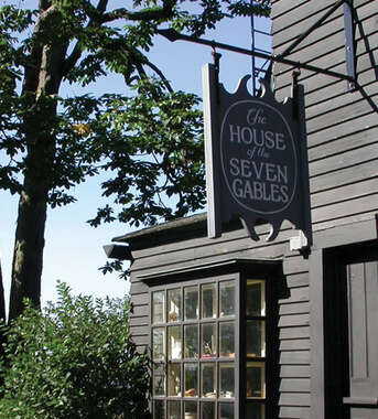 A sign for The House of the Seven Gables hangs on the dark wooden exterior of the historic landmark in Salem, Massachusetts.