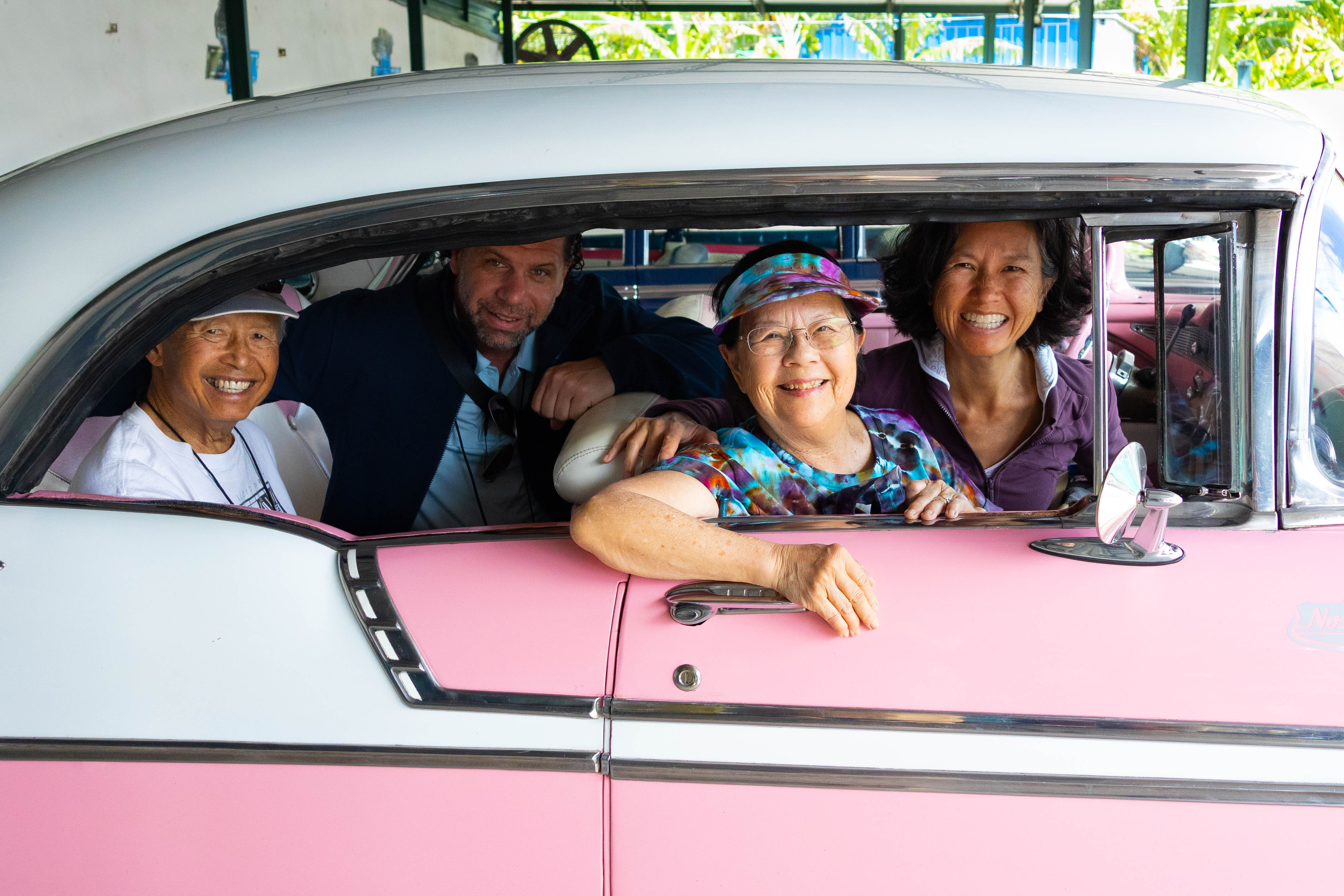 A diverse group of four smiling friends enjoys a fun rideshare together in a classic pink and white car.