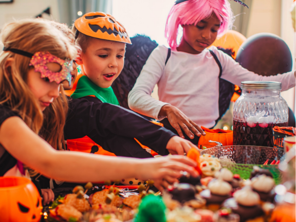Image of kids dressed up for Halloween around a table with Halloween treats and decorations.