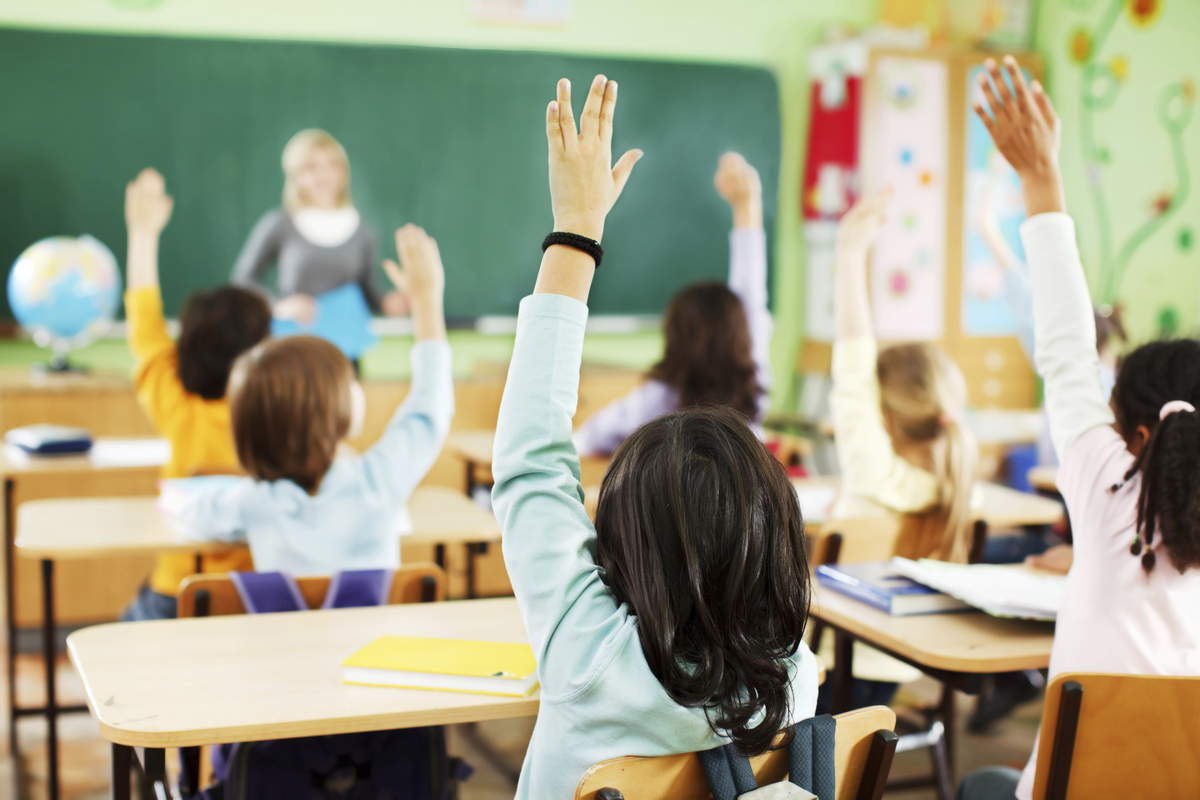 kids & teacher in classroom with hands raised 