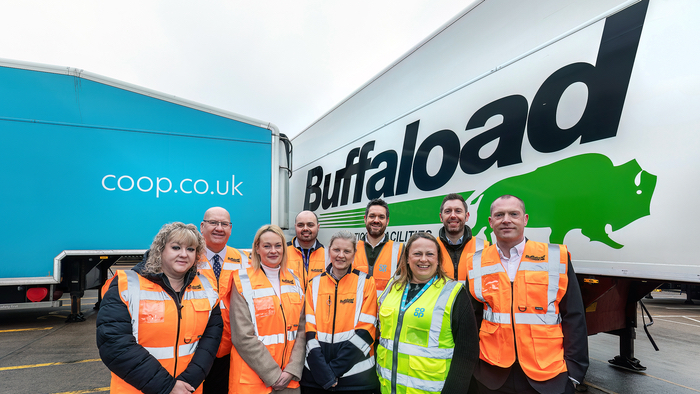 9 people in high-vis jackets standing in front of two trucks. The truck on the left is Co-op branded with a light blue background, and the truck on the right has Buffaload logo on it with a white background. The image depicts the partnership between the two companies.