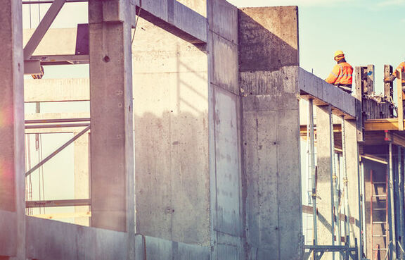 Construction site with workers standing on the top of concrete walls and pillars 