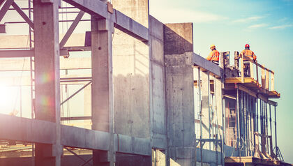 Construction site with workers standing on the top of concrete walls and pillars 