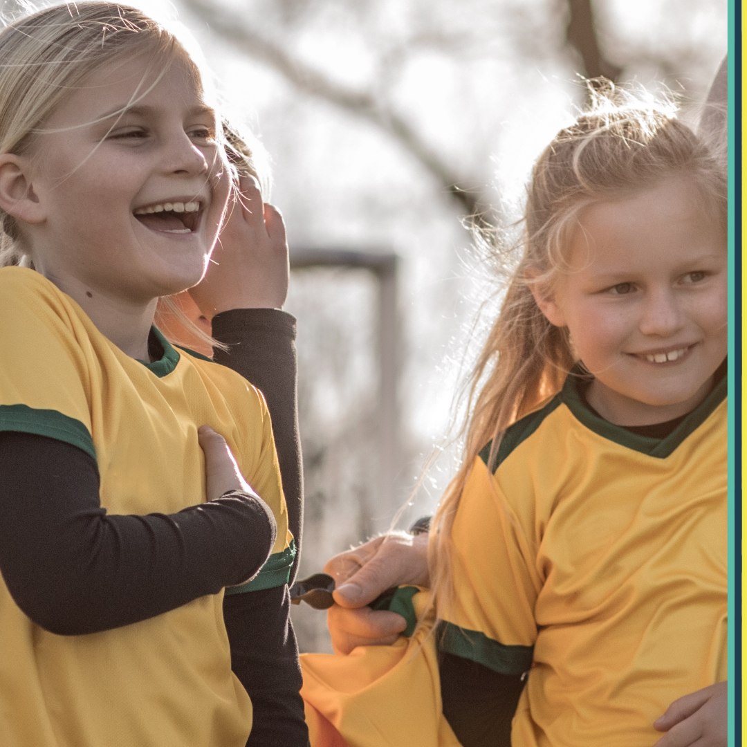 Two little girls smiling and laughing outside on a soccer field in uniform 