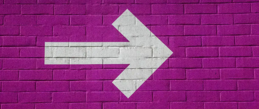 A large, thick white arrow points to the right, painted on a purple brick wall.