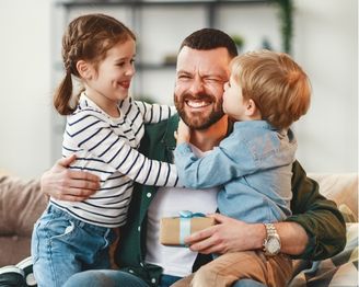 Dad sharing a hug with two children while holding a Father’s Day gift.