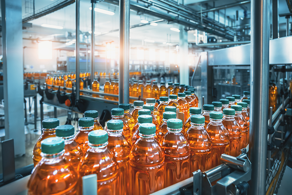 A modern beverage bottling factory with rows of orange-colored liquid-filled plastic bottles with green caps moving along a conveyor belt