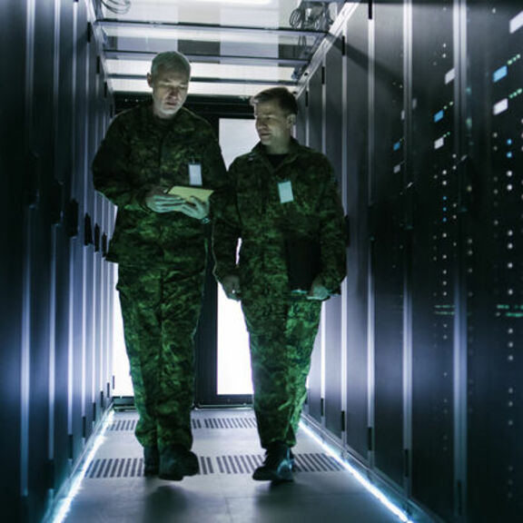 Two service members walking between banks of servers
