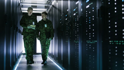 Two service members walking between banks of servers