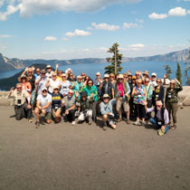 A large group of people poses for a photograph overlooking the blue waters of Crater Lake in Oregon.