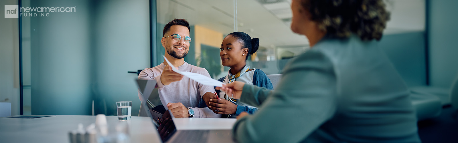 A smiling couple receives paperwork from a loan officer.