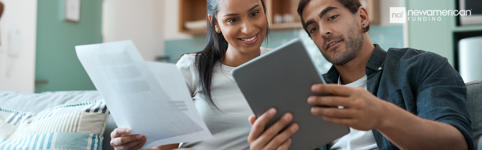 An Asian man and woman sit on a couch in their home going over paperwork 