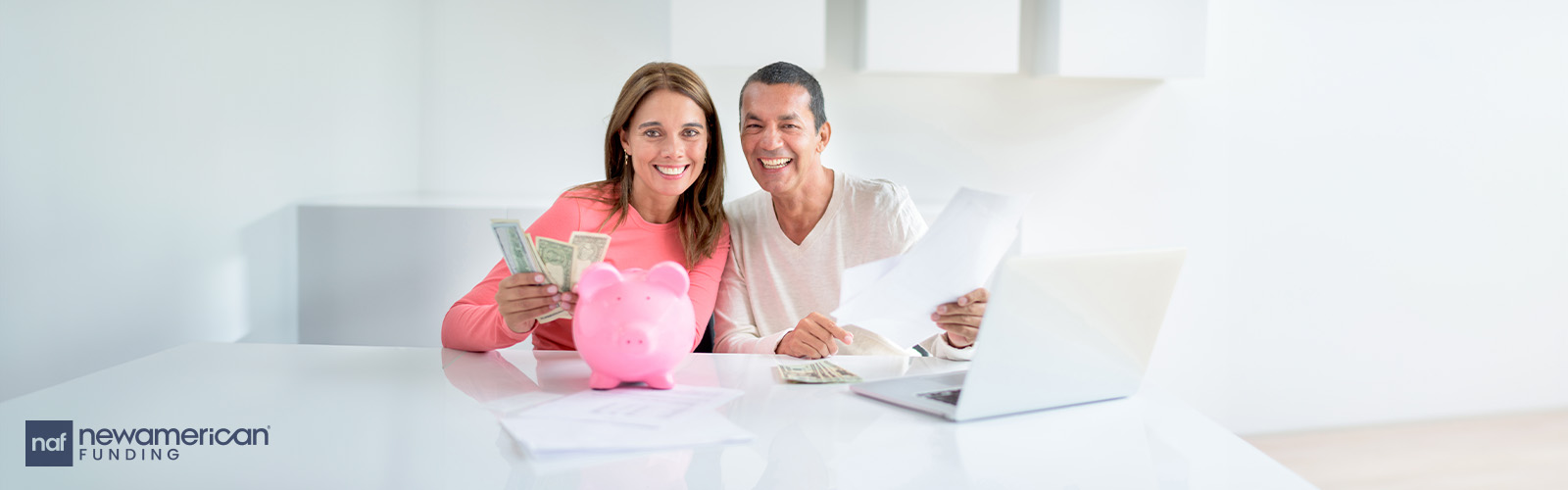 A smiling couple with a laptop and a piggy bank. The woman is holding up cash.