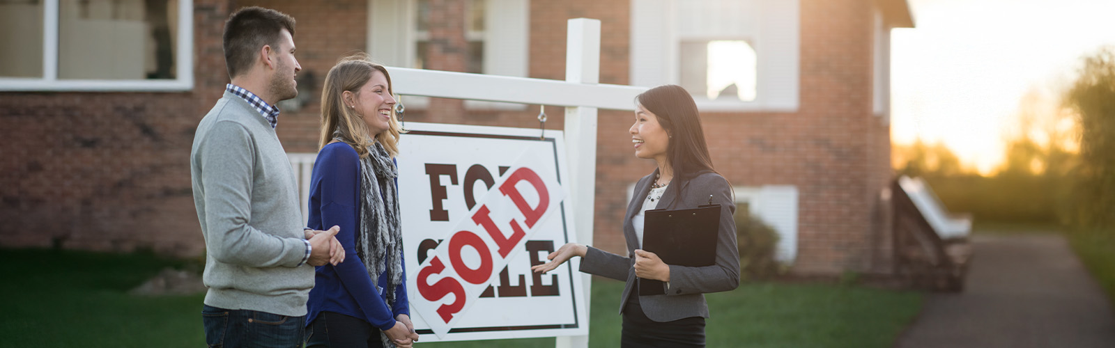 A couple talking to their real estate agent in front of a home sold sign