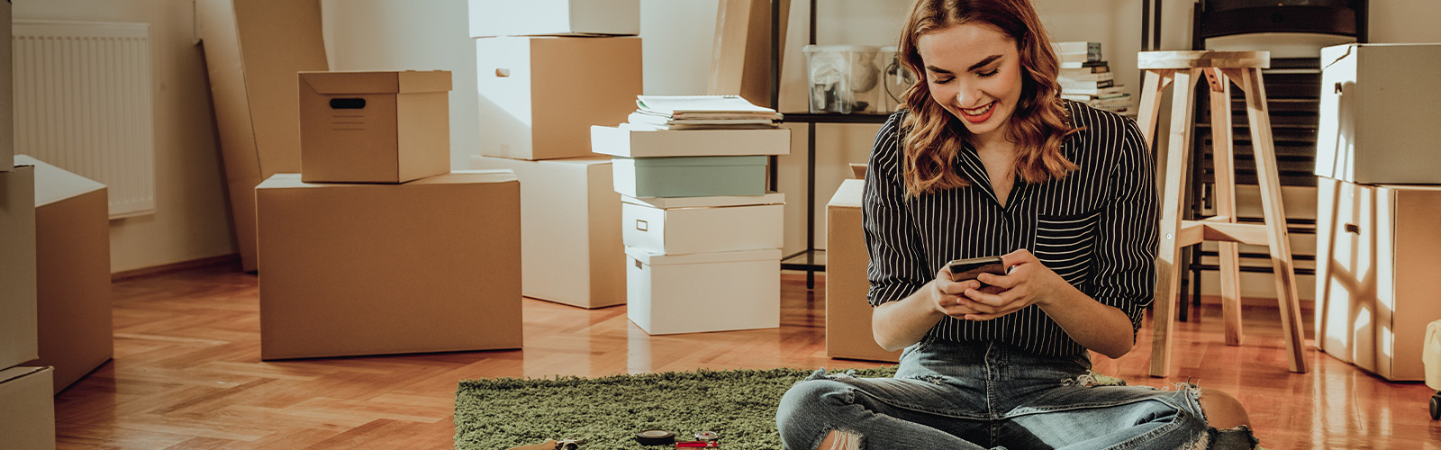 Young woman sitting on the floor of her new home and looking at something on her cell phone