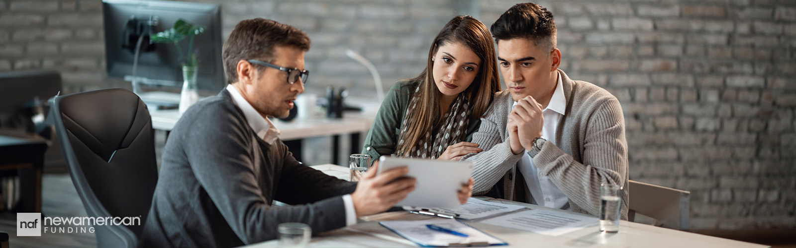 A couple sitting at a desk looks at paperwork with a professional.