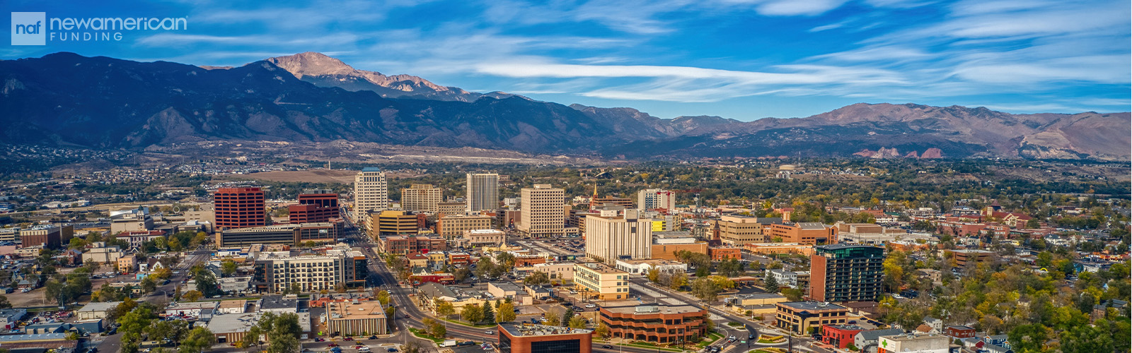 A landscape view of Colorado Springs, CO. The Rocky Mountains rise into the sky behind the city.