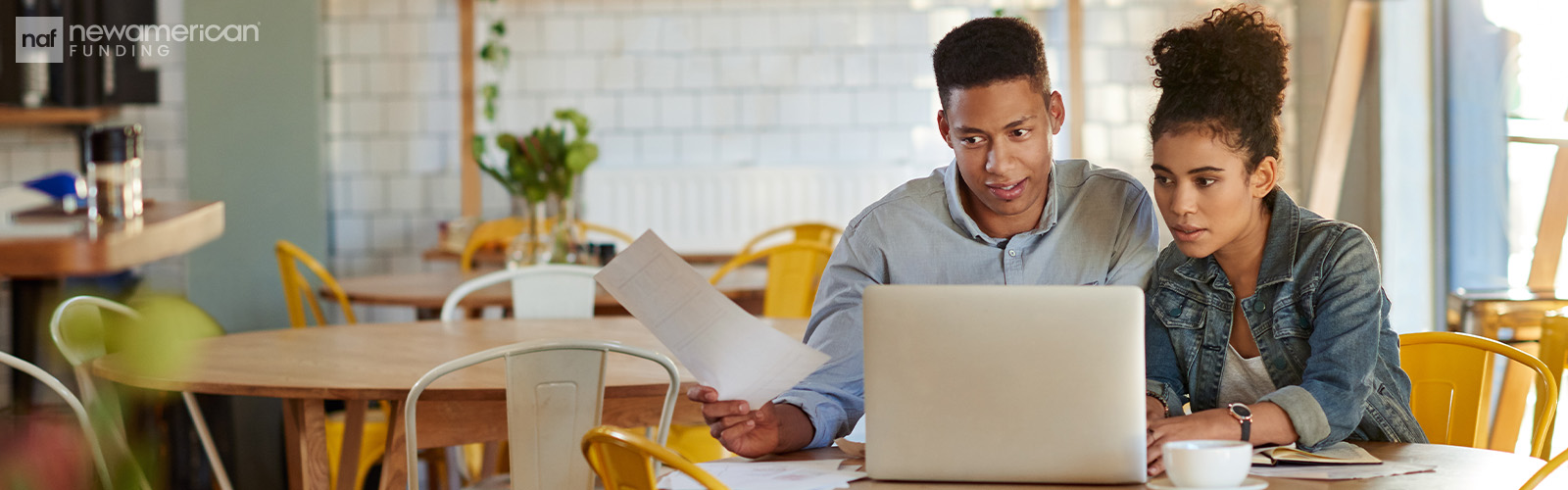 A Black couple sits at a table with papers and a laptop