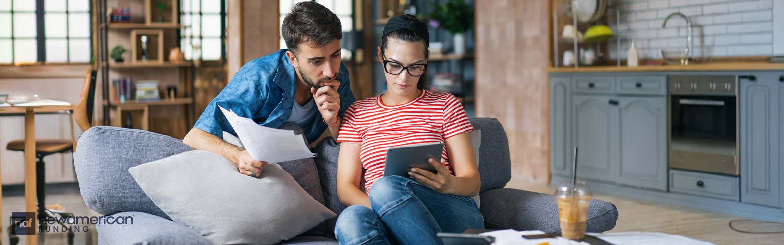 A couple on the couch looks at paperwork and a tablet.