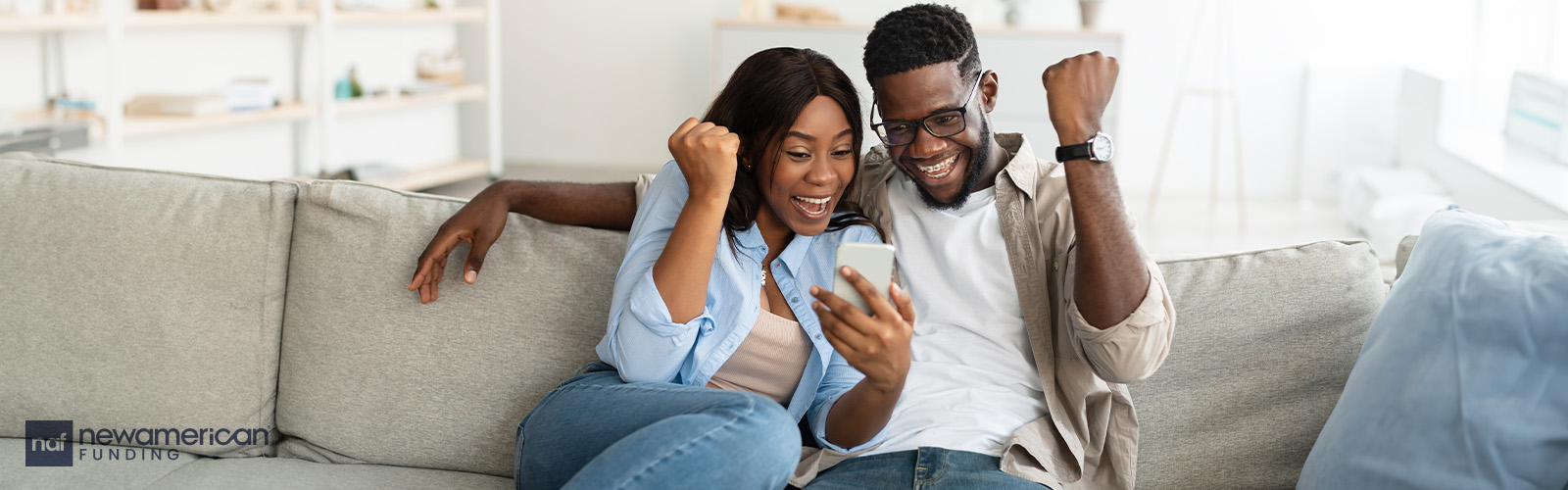 A Black couple celebrates on a couch.
