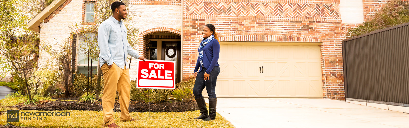 A couple standing by a 'For Sale' sign in front of a brick house.
