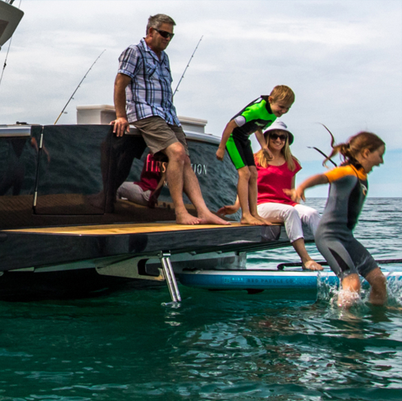 Young girl jumping into the sea from the rear platform of a powerboat as her family looks on