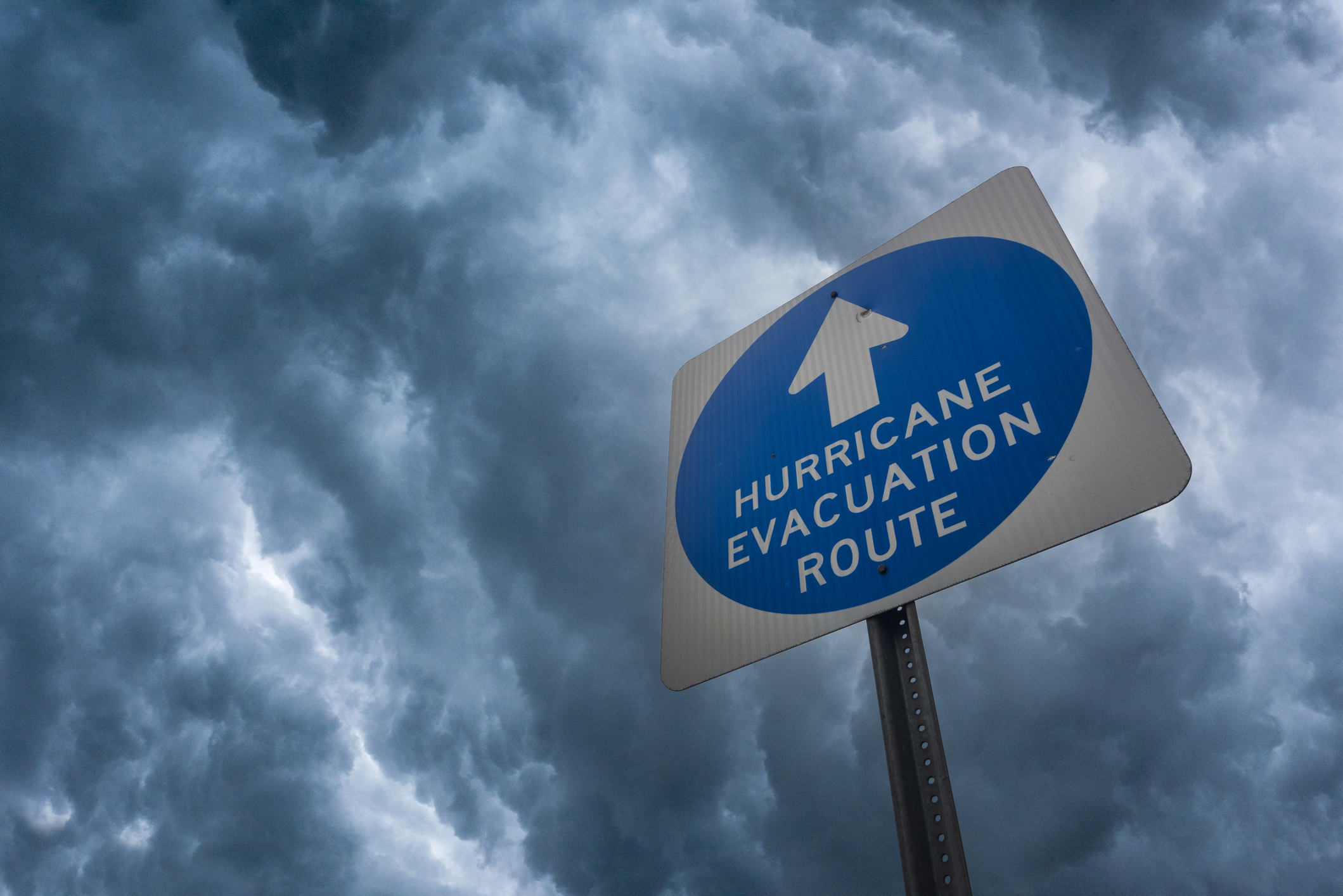 Composite image of a hurricane evacuation route sign against a stormy sky.