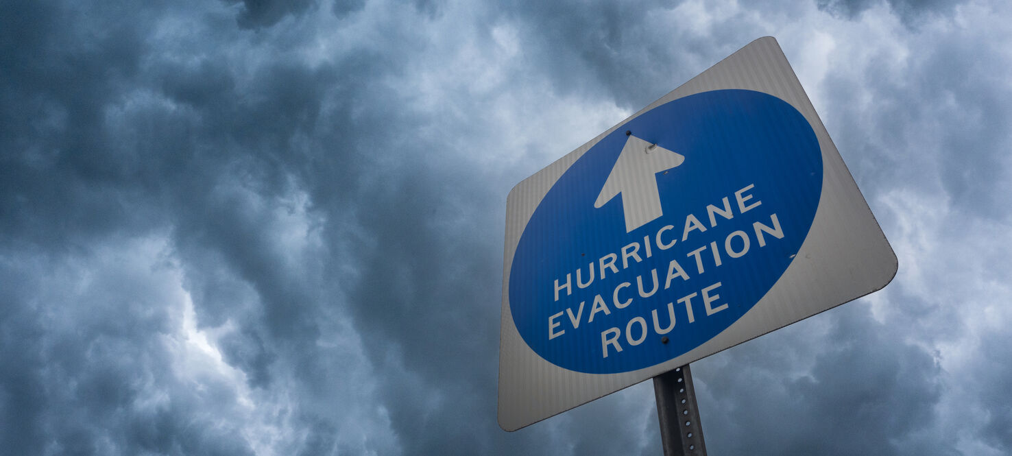 Composite image of a hurricane evacuation route sign against a stormy sky.