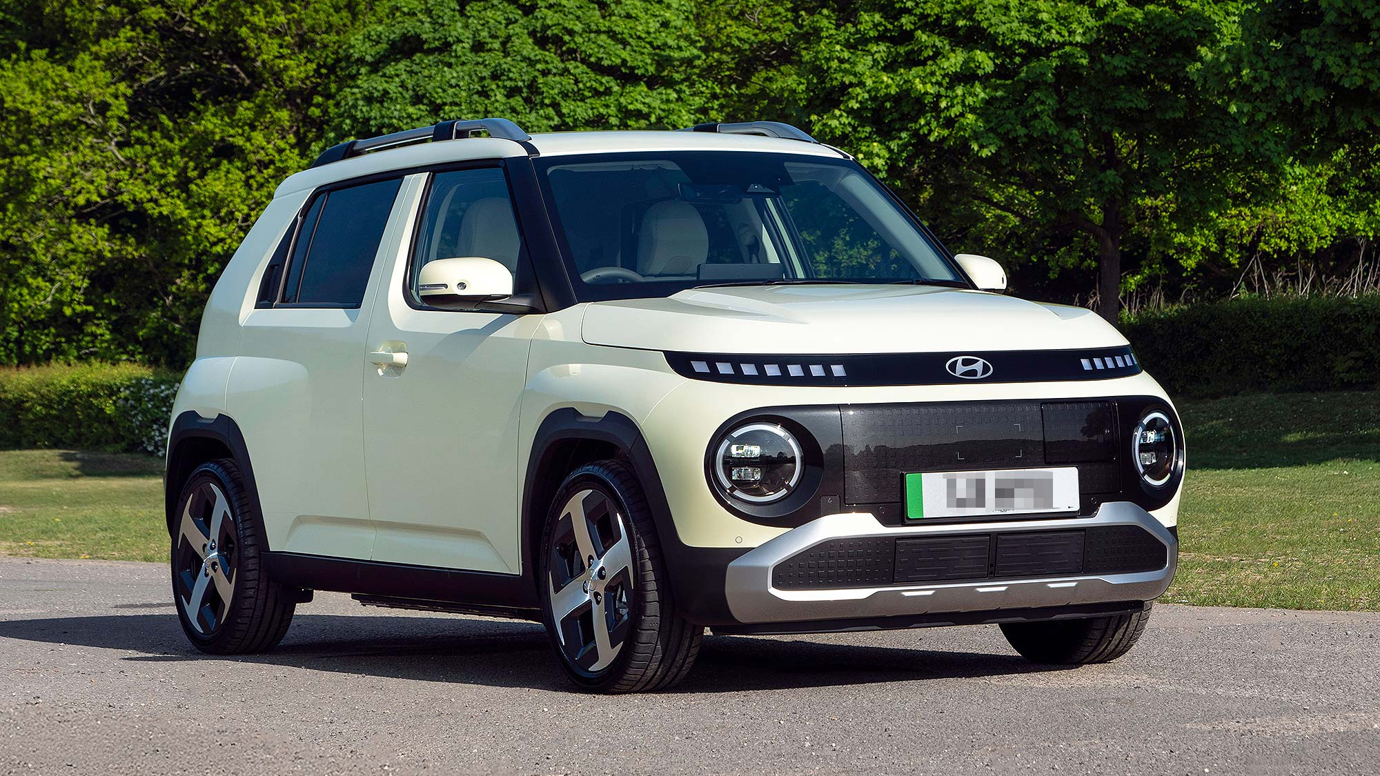 Cream Hyundai Inster compact electric SUV driving along a road, shown from the front left with a blurred background.