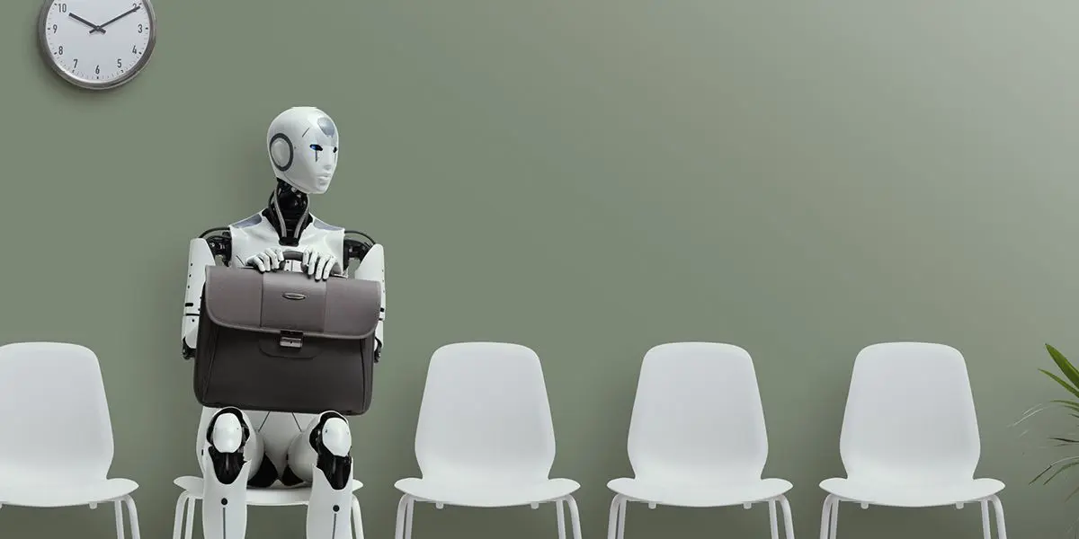 
A humanoid robot, designed with white and black components, is seated in a waiting room holding a dark grey briefcase on its lap. It is positioned in a row of several identical empty white plastic chairs against a plain light green wall. A wall clock is visible in the upper left corner. The image symbolizes the impact of AI and automation on jobs.