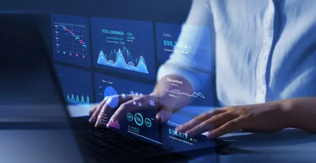 Person working on a laptop with digital data dashboards and analytics charts projected on a screen."
