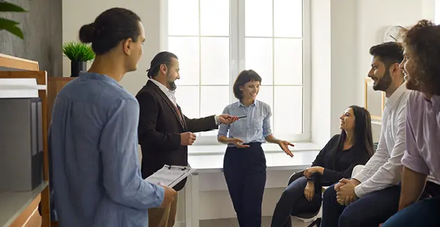 6 people in business wear standing and sitting around a room engaging with each other
