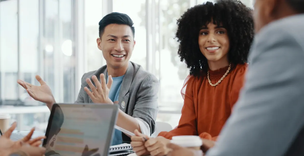 People looking engaged and smiling at a meeting table in a room with lots of light and big windows