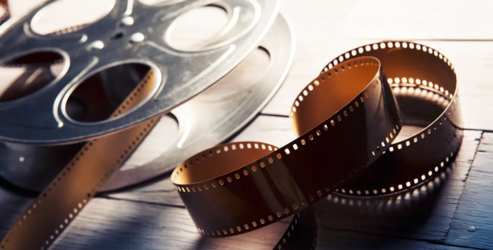An old fashioned movie reel with film coming out and also sat next to the metal reel on a desk 