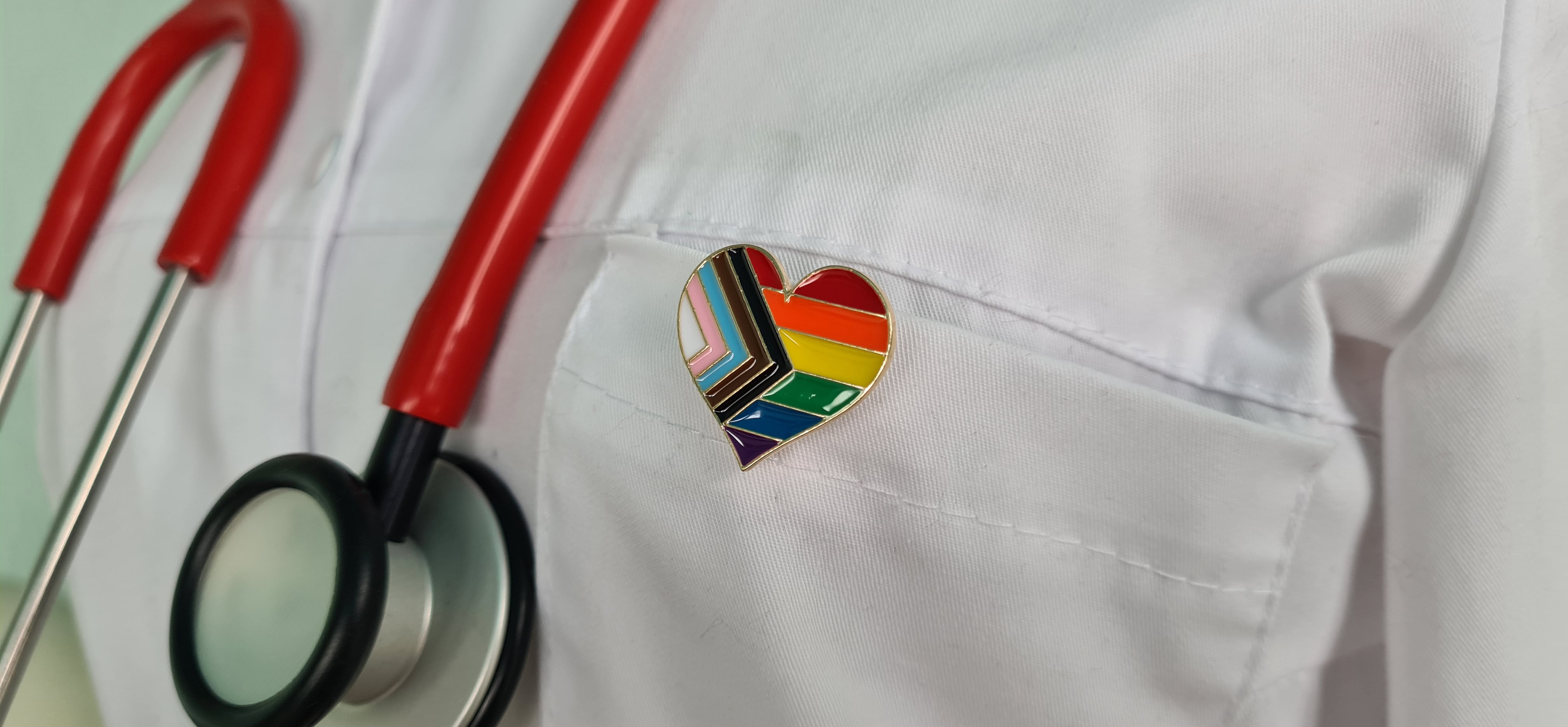 A doctor's coat displays a Progressive Pride pin in the shape of a heart.