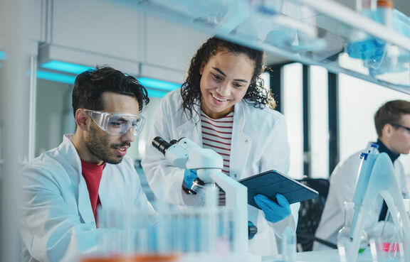 Group of professionals in white lab coats looking at microscopes in a laboratory 