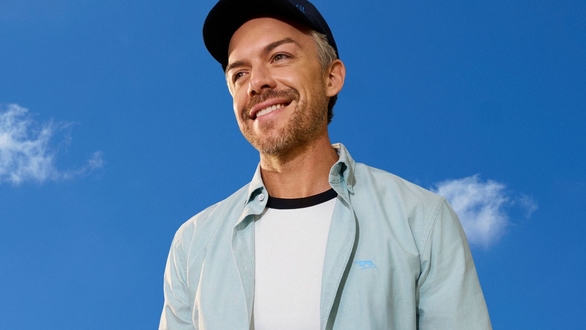 An image of a smiling man wearing a cap and dressed for spring.