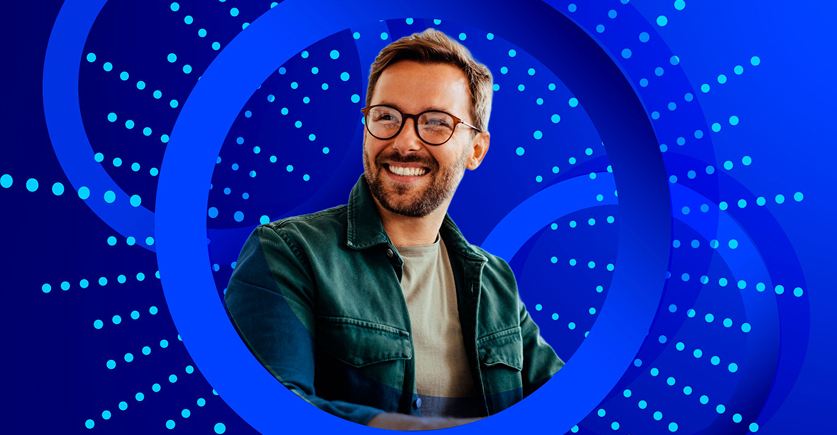 A smiling man with a beard and glasses, wearing a dark green jacket, is framed by