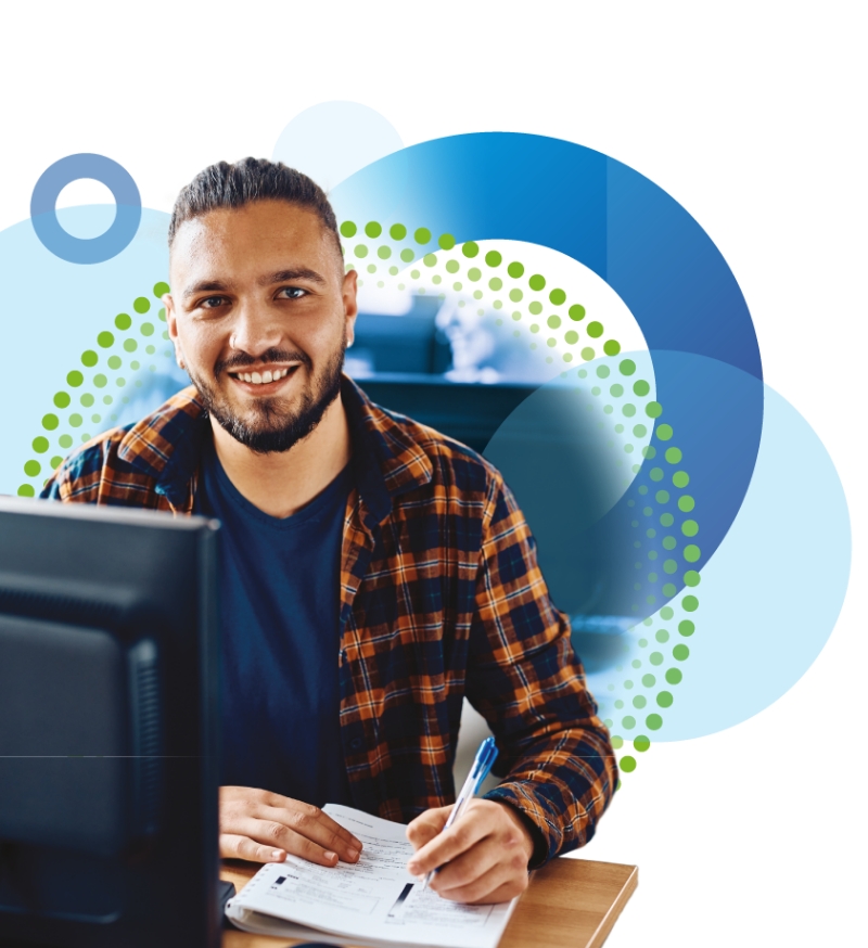 A smiling man with a beard sits at a desk, writing, with abstract blue and green shapes in the background.
